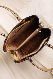 An overhead close-up of a structured handbag interior showing a black exterior, gold-tone hardware, and a brown satin-lined compartment with a zip pocket.