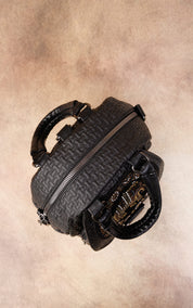 A black quilted leather handbag with a top zipper and double top handles, photographed from a top-down angle on a textured beige background.