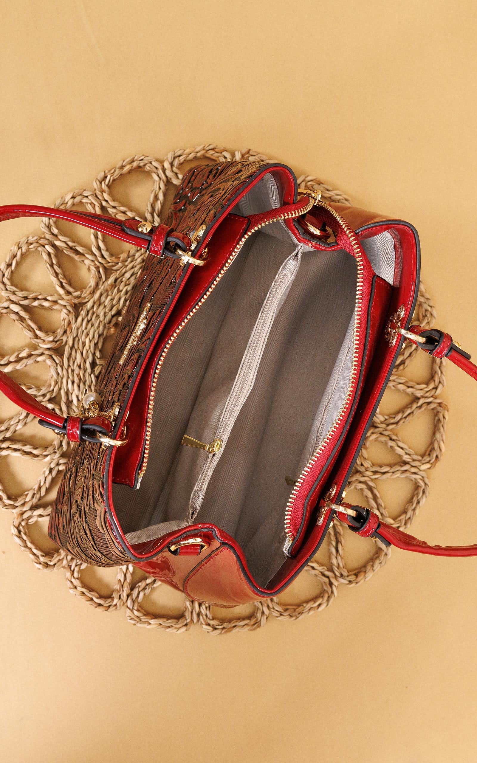 A top-down view of a brown woven tote bag with red leather trim and handles, shown open to reveal a gray interior, placed on a beige background.