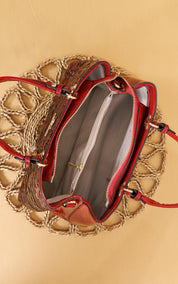 A top-down view of a brown woven tote bag with red leather trim and handles, shown open to reveal a gray interior, placed on a beige background.