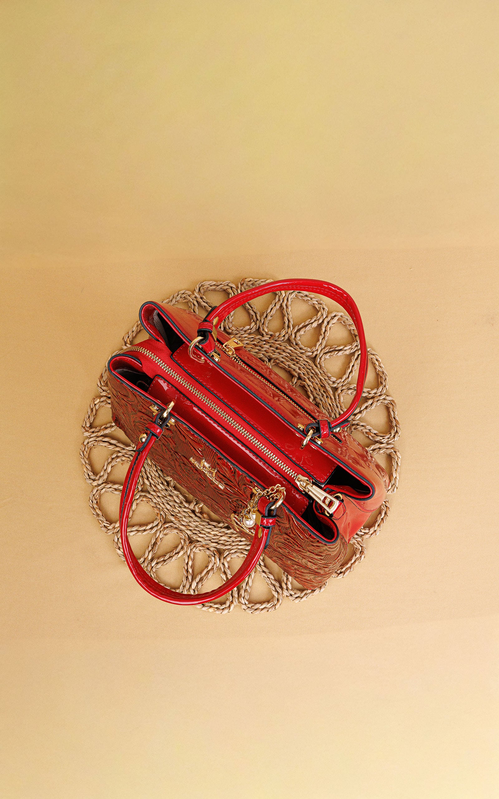 A red leather handbag with gold-tone hardware, displayed from a top-down view on a circular woven placemat against a solid beige background.