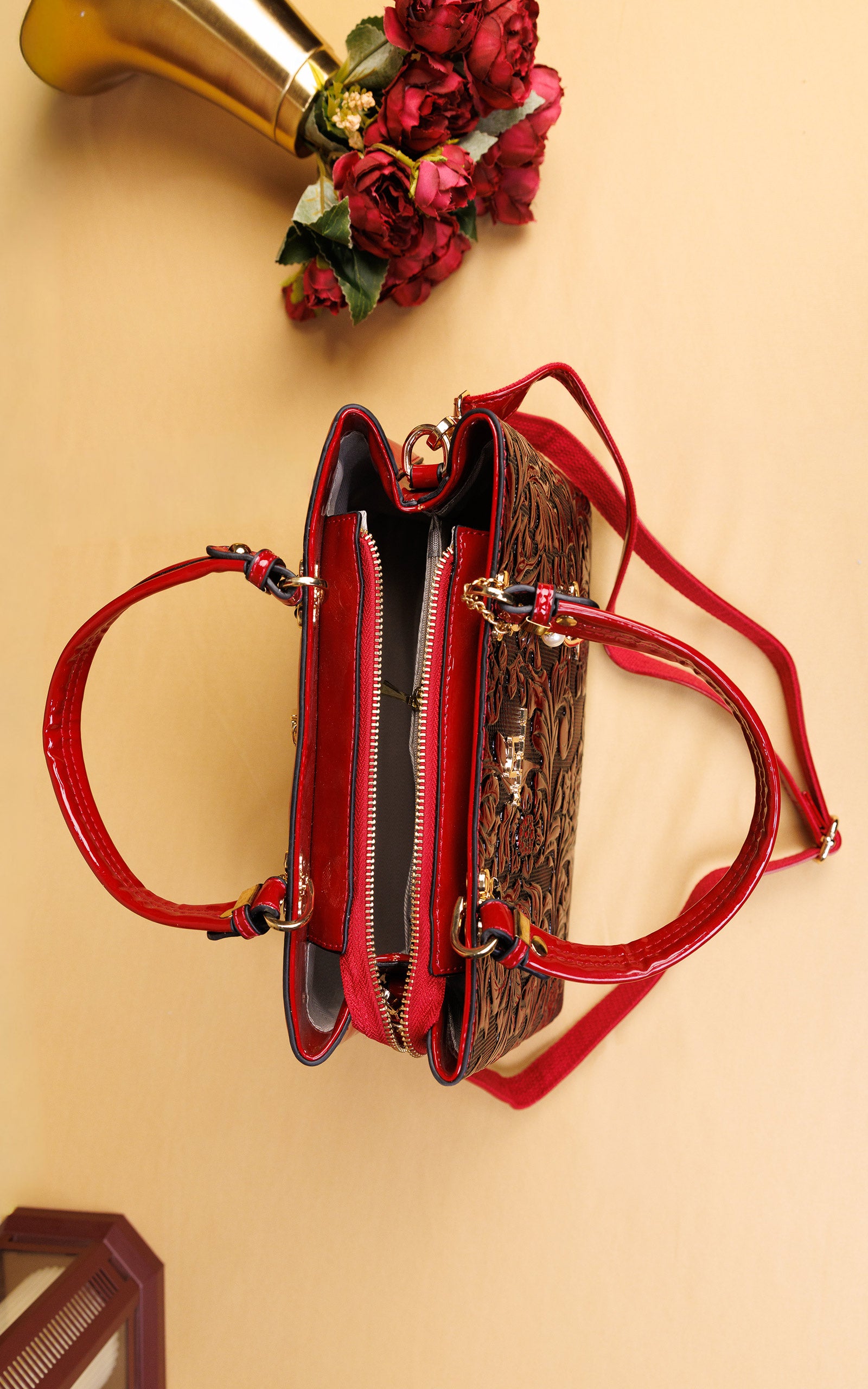 A structured handbag with a glossy red patent leather trim and handles, combined with a brown leopard print body, shown from a top-down view on a beige background with decorative red roses.