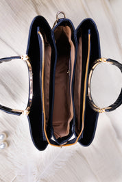 A navy blue structured handbag with gold-tone hardware, shown open from a top-down view on a light textured surface. The bag features three main compartments with gold zippers, a brown interior lining, and decorative pearl-like beads near the bottom left.