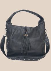 Black handbag with tassel and studs on a beige background back view